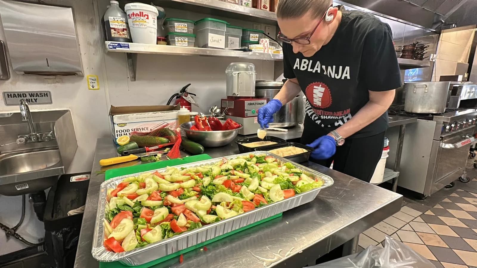 Team member preparing a fresh salad catering tray with cucumber and tomato at Istanbul Mediterranean 2